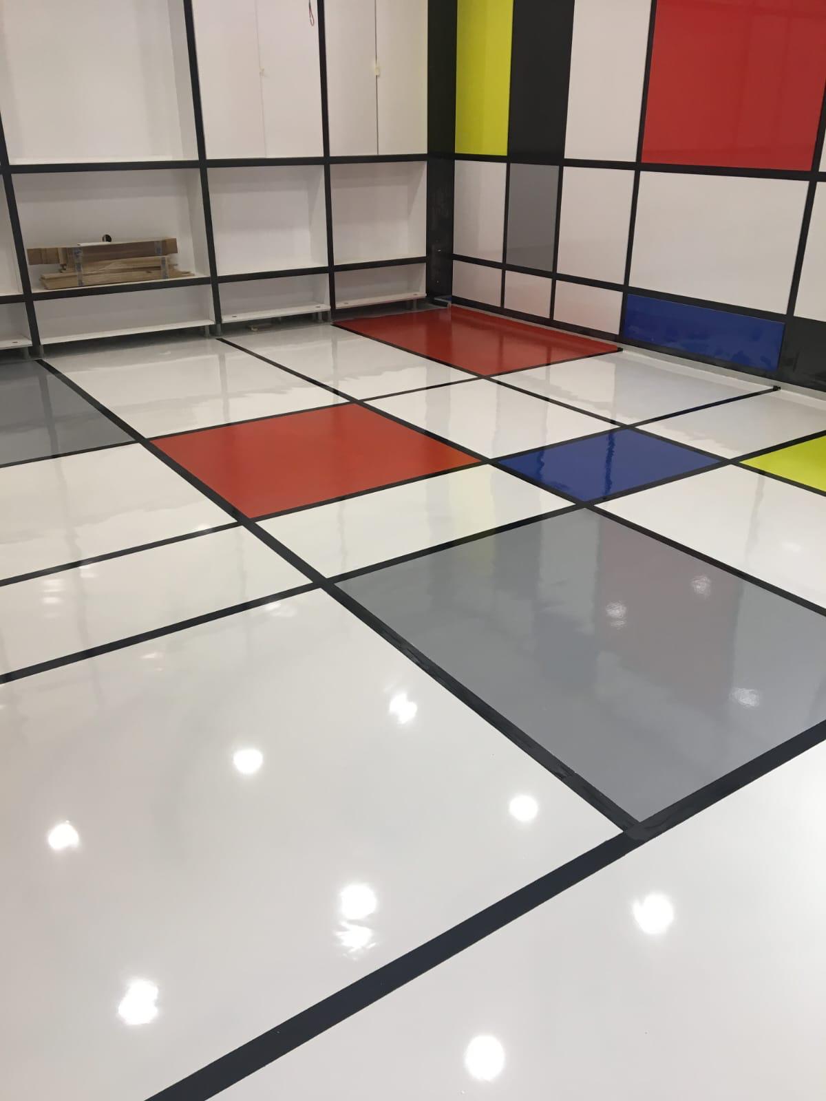 Beyaz zemin üzerine siyah derz çizgileri ve kırmızı, mavi, sarı, gri renk bloklarıyla Mondrian tarzı parlak dekoratif epoksi zemin uygulaması